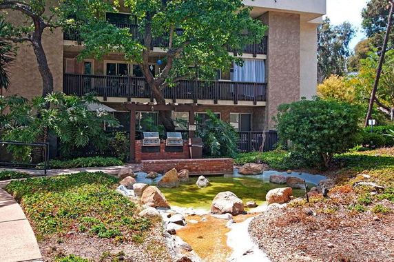 Front view of a multi-story building with balconies surrounded by greenery.