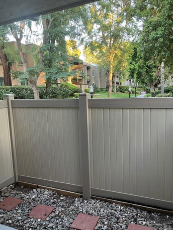 View of buildings and trees seen over a fence from a patio.