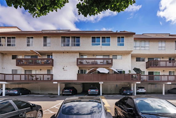 Front view of a multi-story residential building with balconies and a covered parking area.