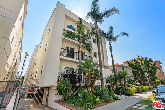 Front view of a multi-story building with balconies and palm trees.