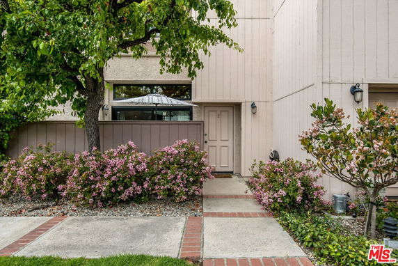 Front view of a two-story house with a pathway and flowering shrubs.