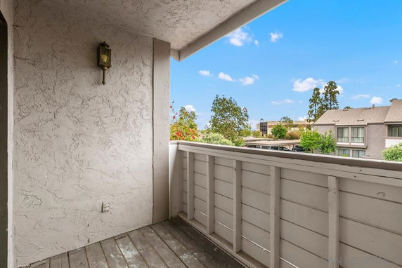 Balcony with wooden railing and view of neighboring buildings and trees.