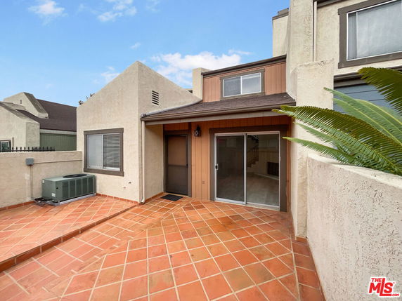 Front view of a house with a patio, sliding door, and light-colored exterior walls.