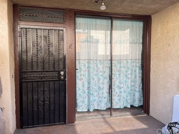 Front view of a building with a metal security door and sliding glass door with floral curtains.