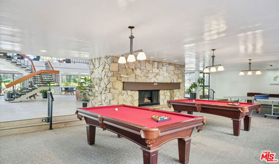 Room with pool tables and stone fireplace in a recreational area.