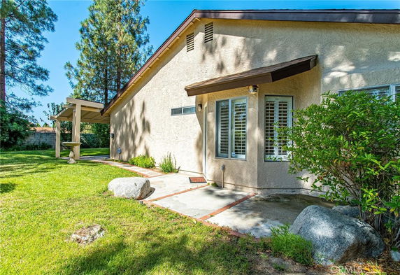 Side view of a single-story house with windows, a small porch, and surrounding greenery.