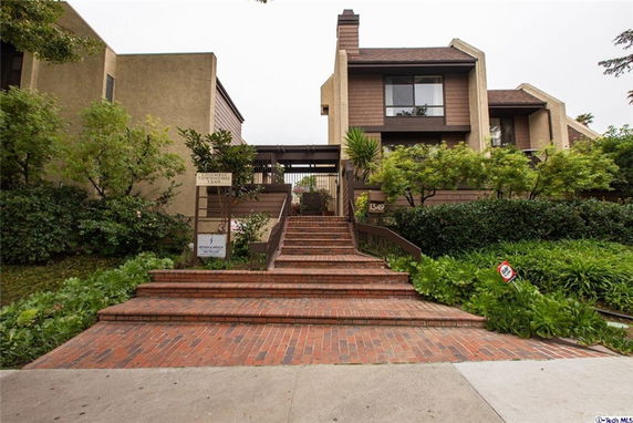 Front view of a multi-story building with brick stairs and lush greenery.