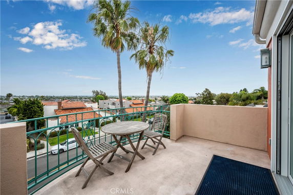 Panoramic view from a balcony showing surrounding residential area with palm trees and blue sky.