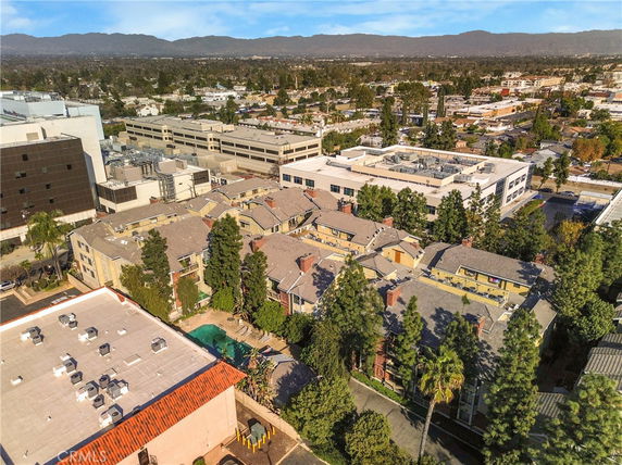 Aerial view of a residential area with multiple buildings surrounded by trees, adjacent to a commercial complex.