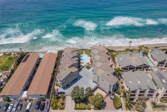 Aerial view of coastal residential buildings with swimming pools, adjacent to the ocean.
