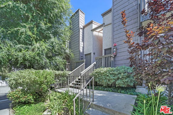 Front view of a multi-story building with stairway entry and surrounding greenery.