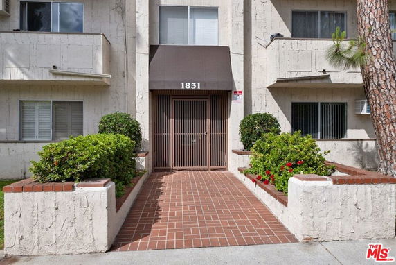 Front view of a multi-story building entrance with brick pathway and plants.
