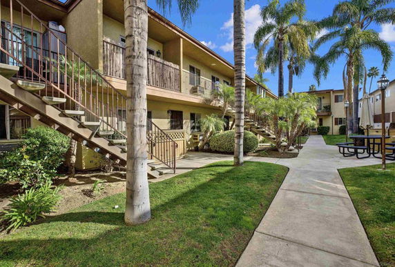 Front view of an apartment complex with exterior staircases and palm trees.