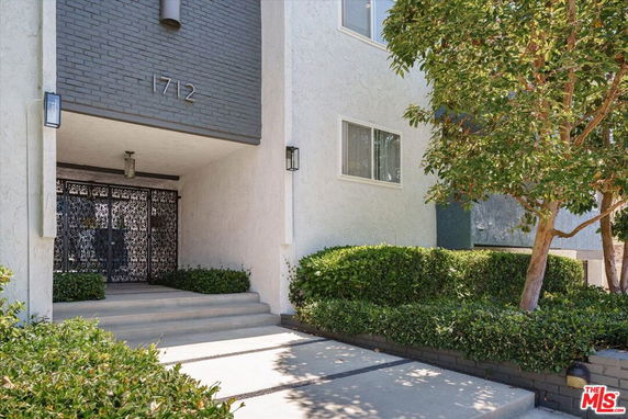 Front view of an apartment building entrance with steps and decorative metal gate.