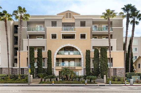 Front view of a multi-story residential building with balconies and palm trees.