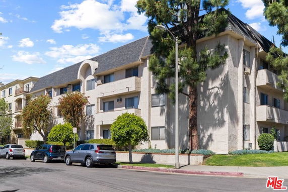 Front view of a multi-story apartment building with a sloped roof and balconies.