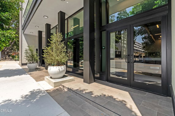 Front view of a modern building with large glass doors and potted plants.