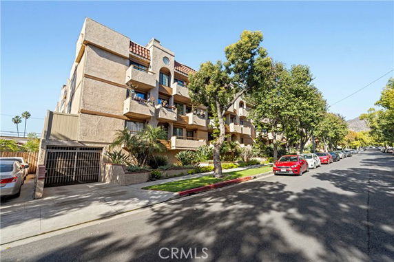 Front view of a multi-story apartment building with balconies and a parking area.