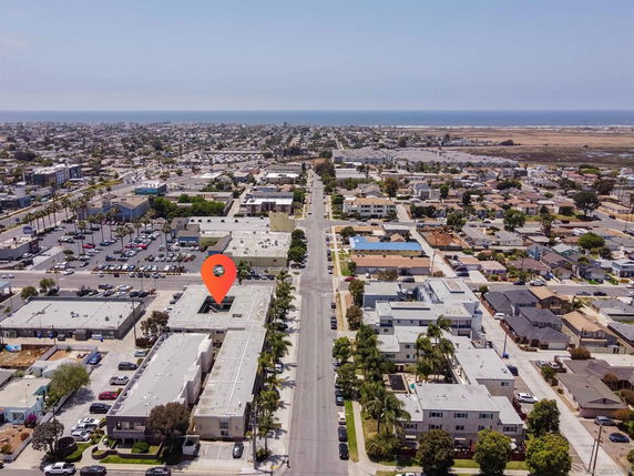 Aerial view of a neighborhood with multiple buildings, roads, and a distant view of the ocean.