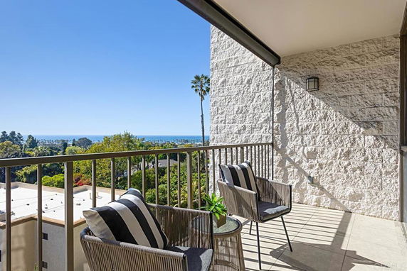Balcony view with seating overlooking greenery and distant ocean.