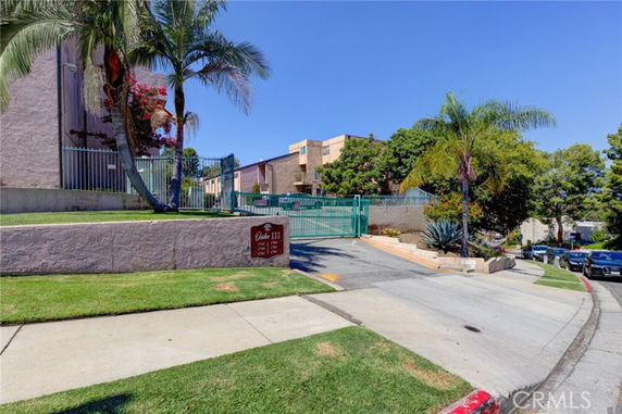 Front view of a multi-story building with a gated entrance and palm trees.
