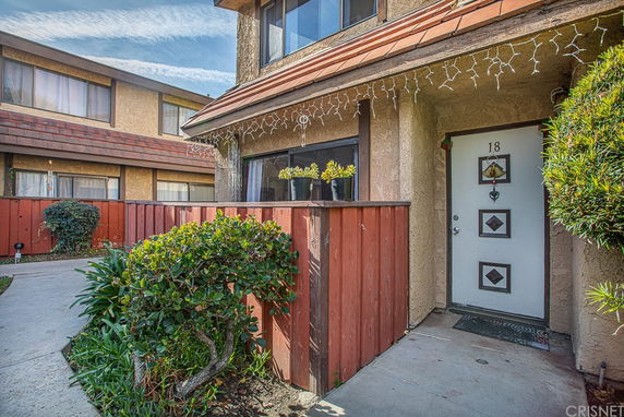 Front view of a two-story townhouse with a small fenced patio and decorative lighting.