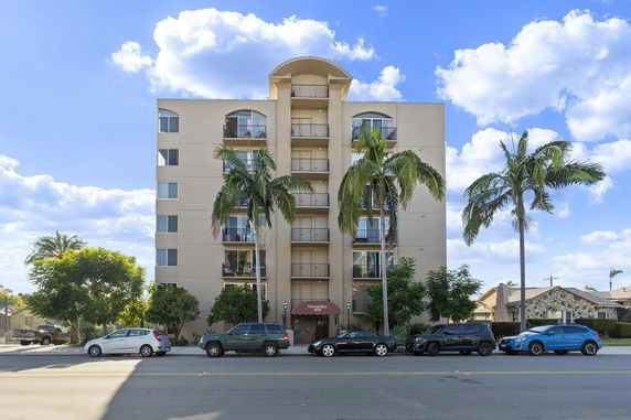 Front view of a multi-story apartment building with balconies and palm trees.