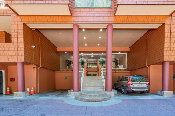 Front view of a building entrance with a stairway and a parked car.