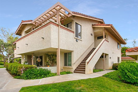 Front view of a two-story house with exterior stairs and a pergola.