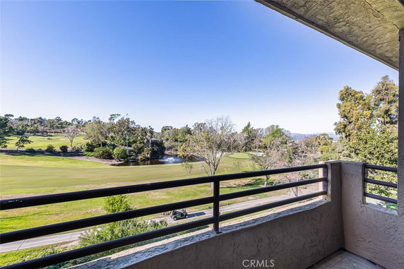 Panoramic view from a building balcony overlooking a golf course and trees.