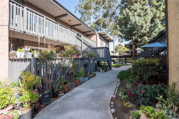 Front view of a multi-story residential building with a wooden railing and a pathway lined with potted plants.