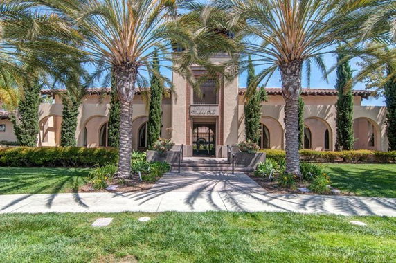 Front view of a building with arched windows and palm trees lining the walkway.