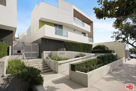 Front view of a modern multi-story building with a gated entrance and landscaped pathway.