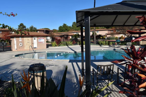 Outdoor swimming pool area with surrounding buildings and seating under a canopy.
