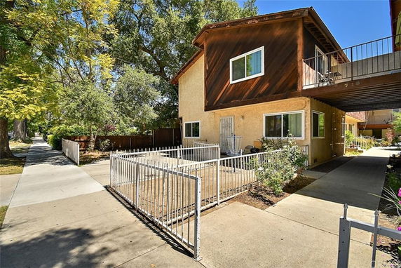 Front view of a two-story house with a balcony and fenced front yard.