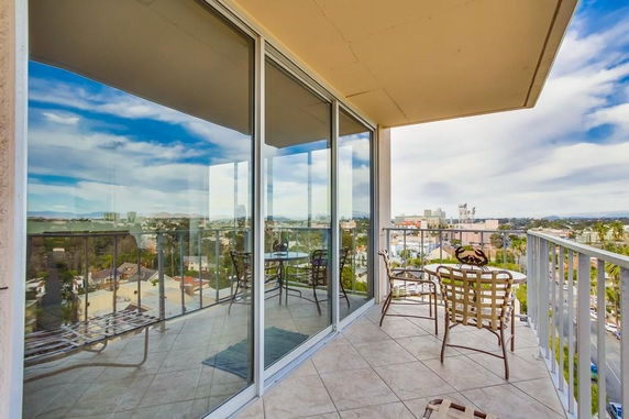 Panoramic view of a cityscape from a balcony with glass railings and outdoor seating.