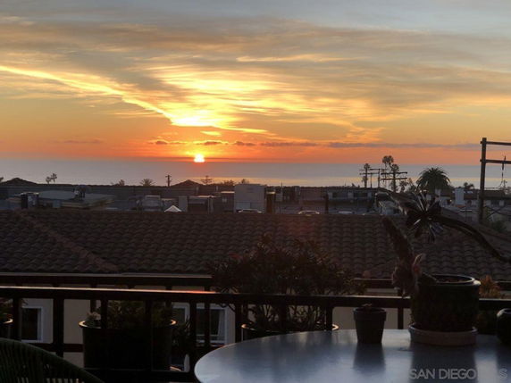 Wide angle view of a sunset over rooftops and ocean.