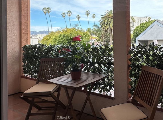 Balcony with chairs and table offering a view of palm trees and distant buildings.