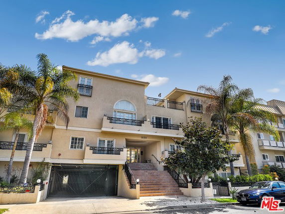 Front view of a multi-story residential building with balconies and a gated entrance.