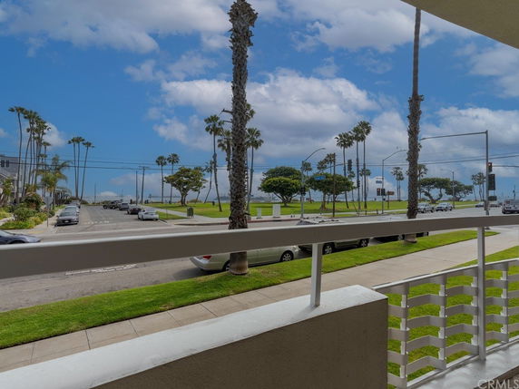 View from a building overlooking a street lined with palm trees and grass, leading to the sea.