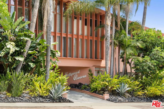 Front view of a mid-century modern building with large vertical windows and lush landscaping.