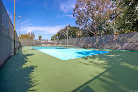 View of an outdoor tennis court surrounded by trees and fencing.