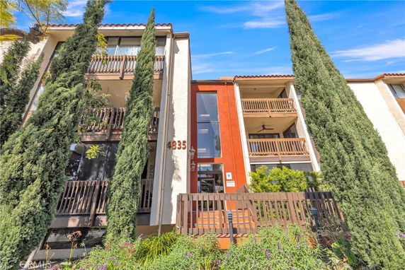 Front view of a multi-story building with balconies and tall trees.