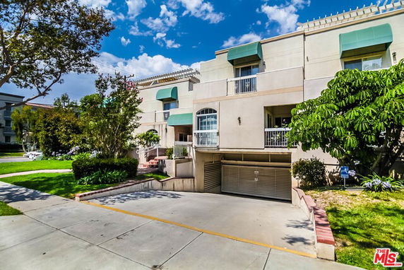 Front view of a multi-story residential building with green awnings and a driveway leading to an underground garage.