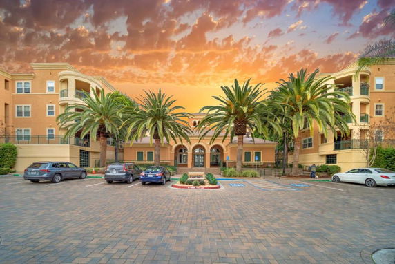 Front view of a multi-story building with palm trees and a parking area in front.