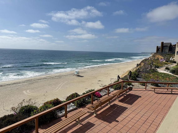 Panoramic view of a beach and ocean from a terrace with benches.