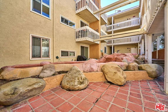 View of a multi-story building with balconies and rock landscaping.