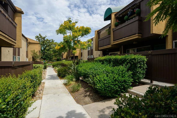 Front view of a multi-story apartment building with balconies and a pathway.