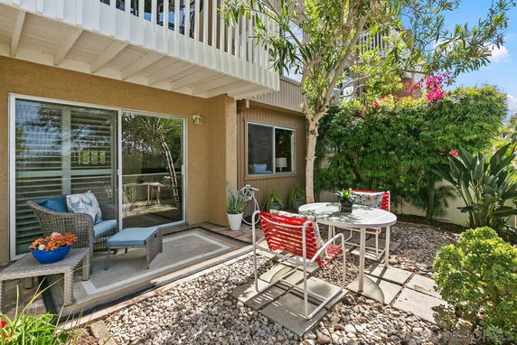 Outdoor patio area with seating and a small table surrounded by greenery and a building with a balcony.