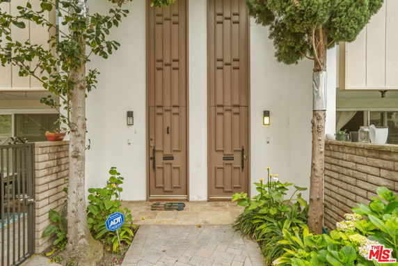 Front view of a house with tall brown double doors and surrounding greenery.